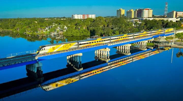 A distant view of a Brightline train crossing a bridge.